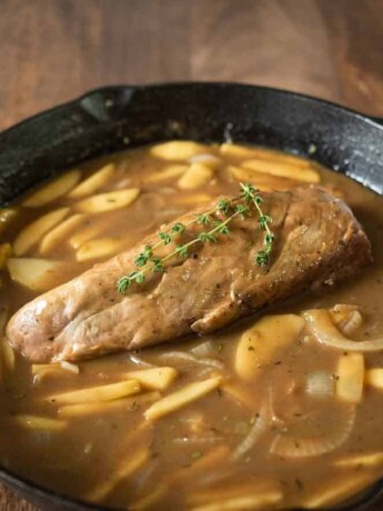 A cast iron skillet with apple and ale gravy and pork tenderloin