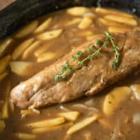 A whole pork tenderloin cooking in gravy with fresh apples