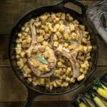 A cast iron skillet with pork chops on a bed of apple salsa