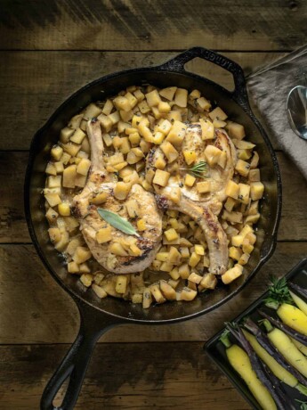 A cast iron skillet with pork chops on a bed of apple salsa