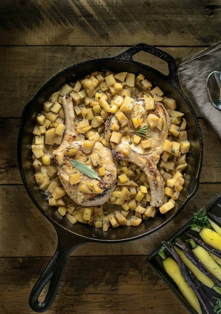 A cast iron skillet with pork chops on a bed of apple salsa