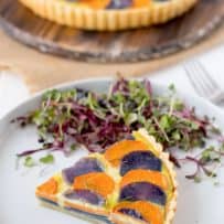 A slice of potato and vegetable quiche on a white plate with micro greens
