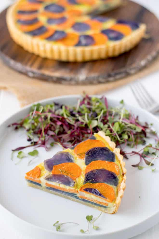 A slice of potato and vegetable quiche on a white plate with micro greens