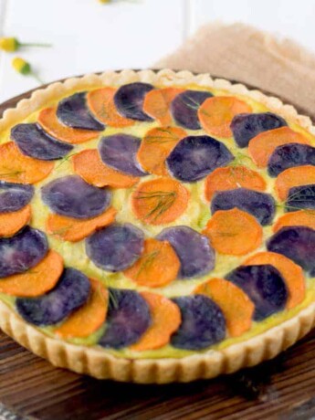 Potato and vegetable quiche topped with slices of orange and purple potatoes
