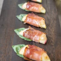 A closeup of apple slices wrapped in prosciutto with basil
