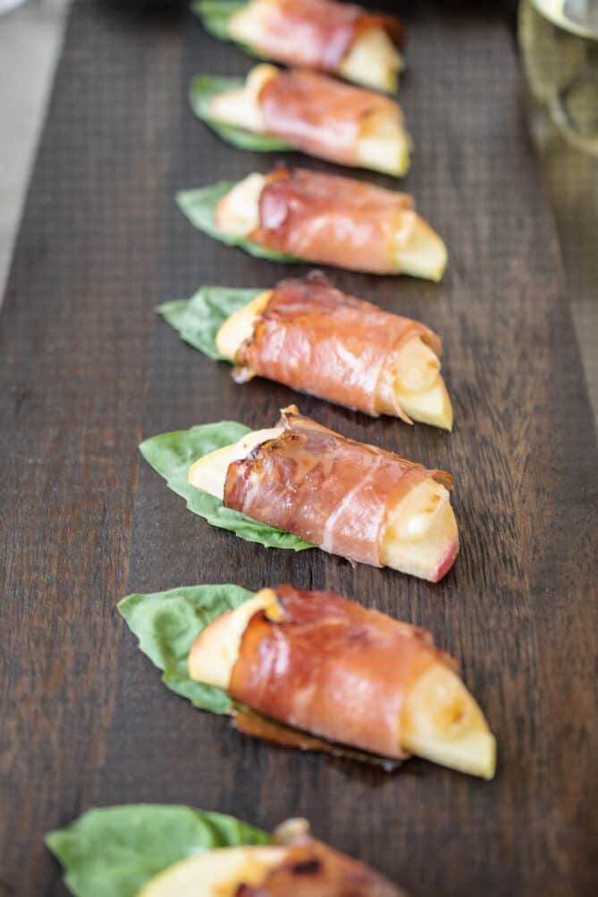A closeup of apple slices wrapped in prosciutto with basil