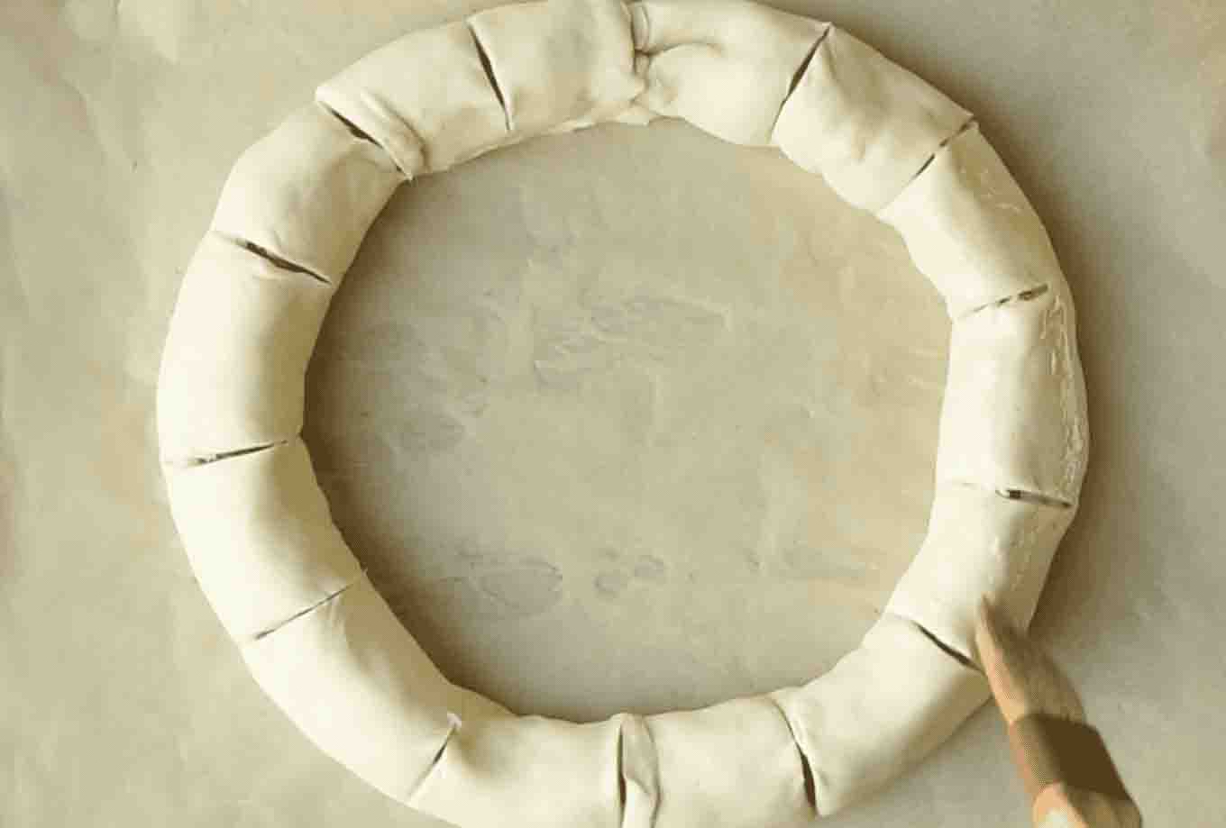 Brushing a sausage roll wreath with egg wash