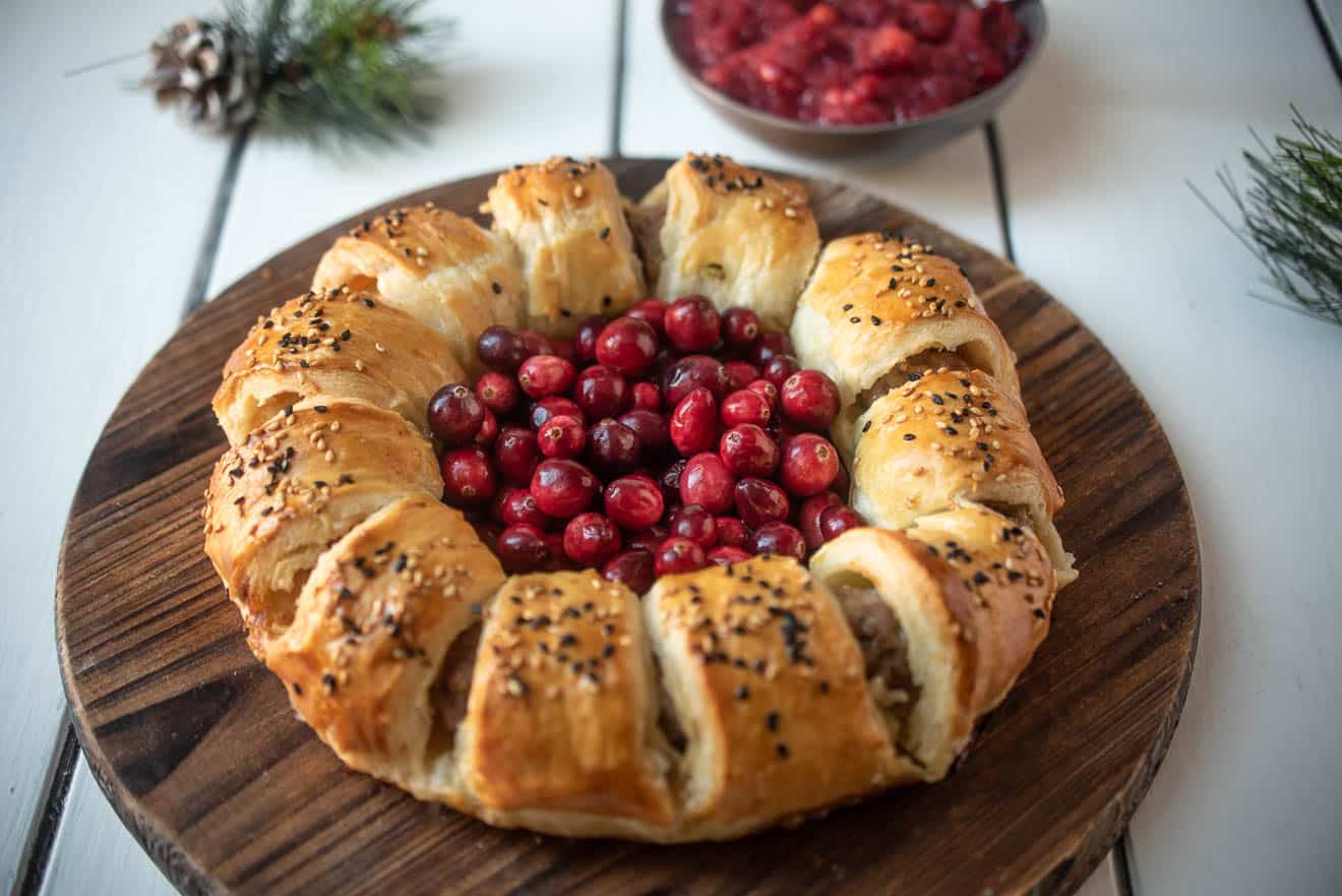 Puff pastry rolled into a wreath shape filled with pork sausage on a board with fresh cranberries in the center