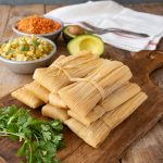 Tamales wrapped in corn husks piled onto a serving board