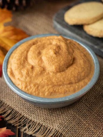 The dip is served in a grey bowl surrounded by shortbread cookies, maple leaves and mini pumpkins