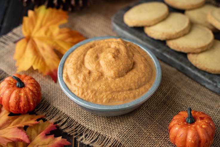 The dip is served in a grey bowl surrounded by shortbread cookies, maple leaves and mini pumpkins