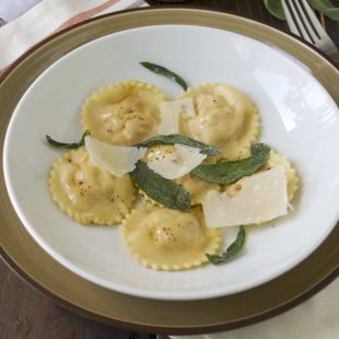6 pumpkin ricotta ravioli on a white plate with crispy sage leaves and shaved Parmesan