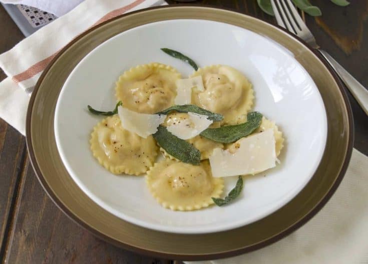 6 pumpkin ricotta ravioli on a white plate with crispy sage leaves and shaved Parmesan