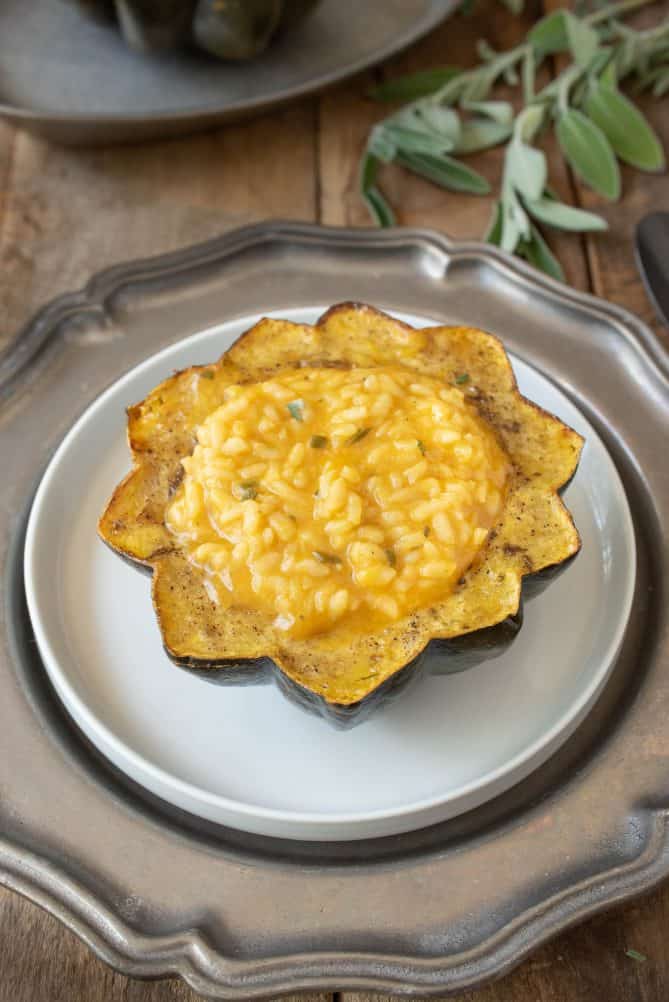 A white plate on top of a pewter plate holding a pumpkin risotto stuffed acorn squash