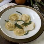 6 round ravioli on a plate with shaved Parmesan and sage