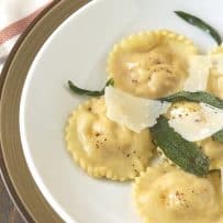 Round pumpkin ricotta ravioli on a white plate with shaved Parmesan and crispy sage