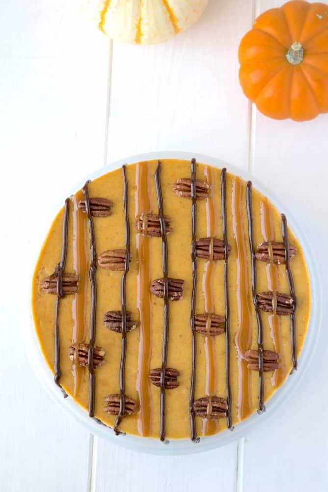 Pumpkin cheesecake from overhead decorated with caramel and chocolate sauce stripes and pecan halves
