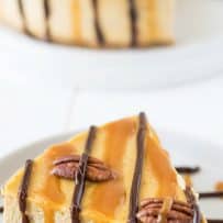 A perfect slice of pumpkin cheesecake with caramel and chocolate on a white plate decorated with chocolate and caramel drizzle