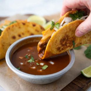 A crispy beef taco being dipped in the sauce used to cook the beef