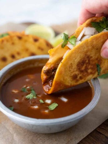 A crispy beef taco being dipped in the sauce used to cook the beef
