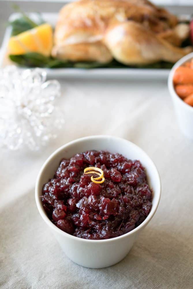 Cranberry sauce garnished with an orange rind in a white serving bowl with a turkey in the background