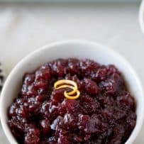 Dark red cranberry sauce in a white bowl topped with an orange rind