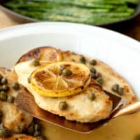 A chicken breast on a spatula with lemon and capers