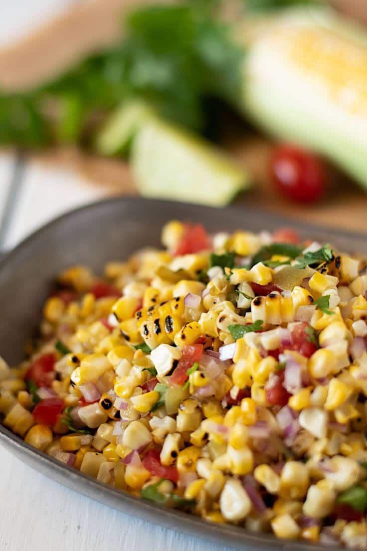 A closeup showing the grilled corn kernels and colorful ingredients in a grey bowl