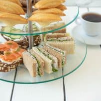 Madeleine cookies and sweet treats in a tiered cake stand with tea sandwiches