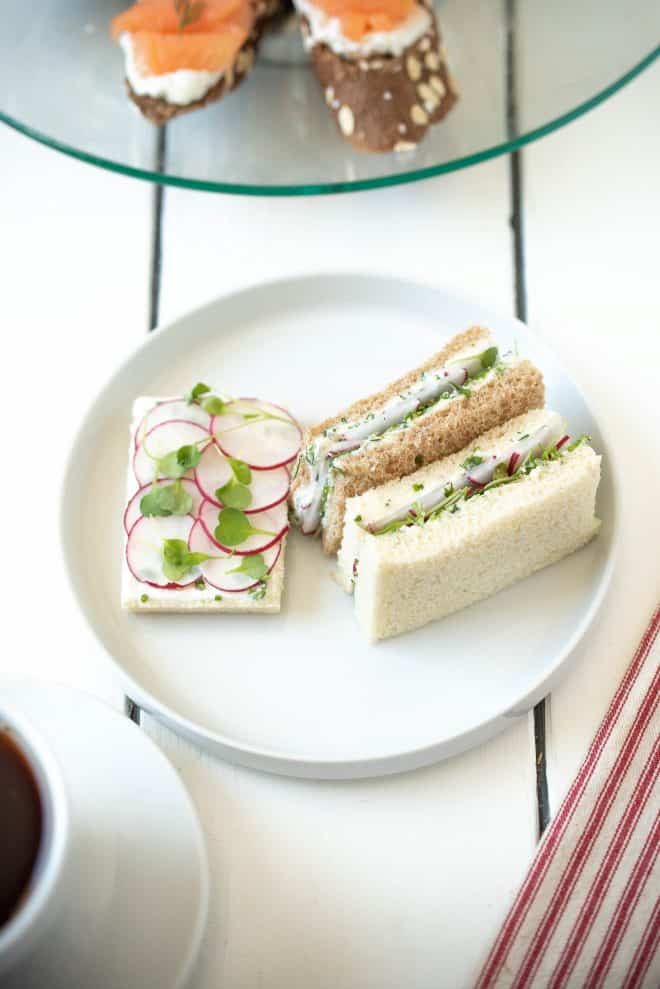 1 open-faced and 2 rectangle, crustless radish and herb butter sandwiches on a round white plate