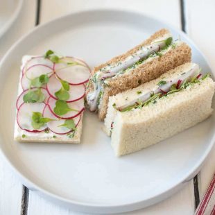 An open faced and mini crustless radish and herb butter sandwiches on a white plate