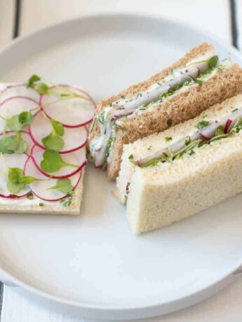 An open faced and mini crustless radish and herb butter sandwiches on a white plate