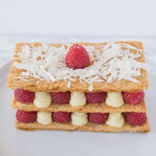 The dessert on a plate showing the red raspberries and lemon custard sandwiched between puff pastry