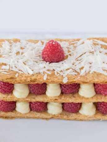 The dessert on a plate showing the red raspberries and lemon custard sandwiched between puff pastry