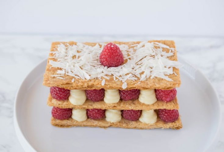 The dessert on a plate showing the red raspberries and lemon custard sandwiched between puff pastry
