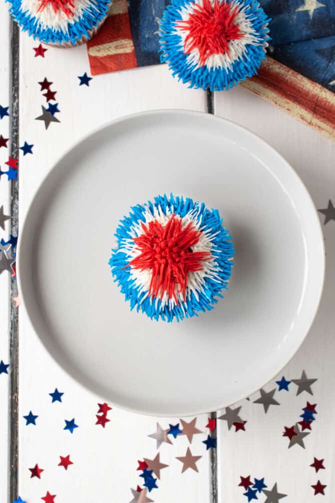 An overhead of a cupcake on a white round plate with red white and blue frosting