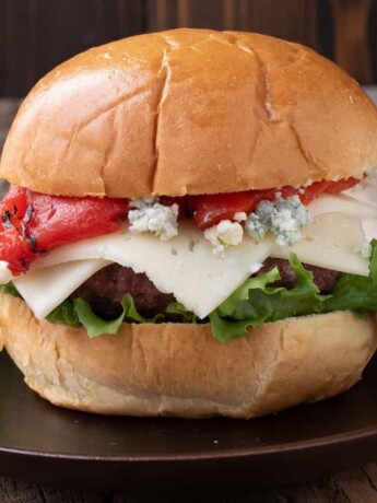 A side view of a burger topped with red pepper, white and blue cheese