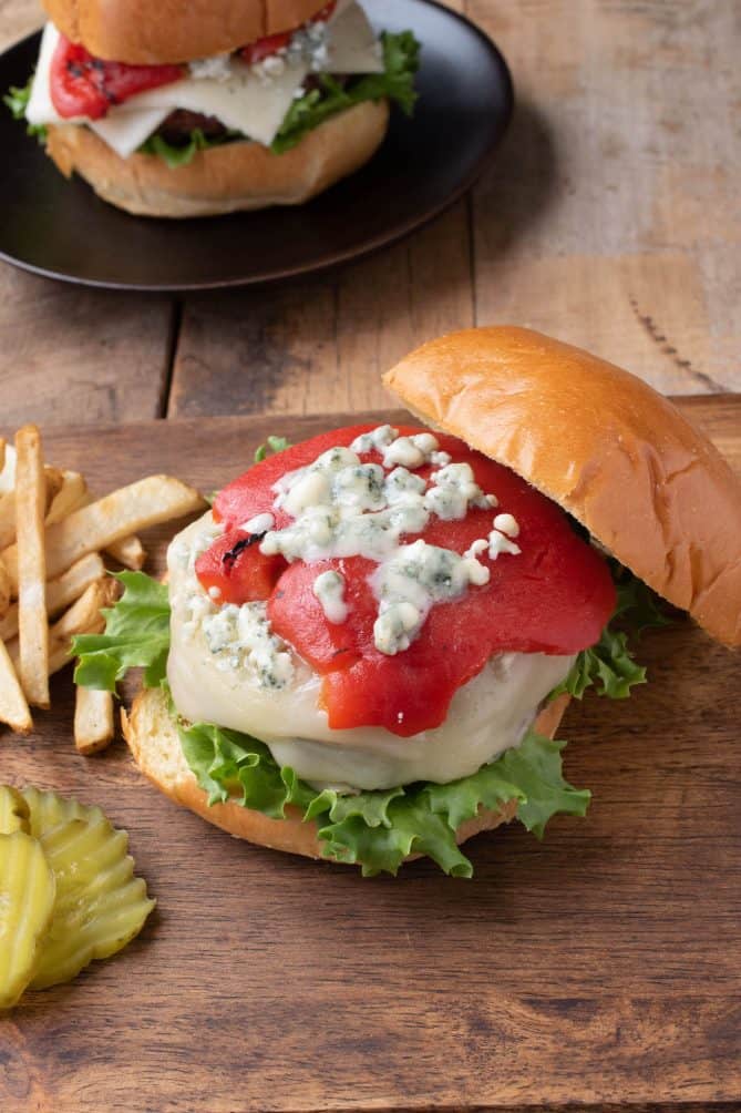 A beef burger topped with melted white cheese, roasted red pepper and blue cheese with fries