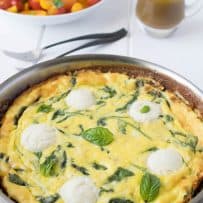 Frittata in a pan topped with fresh ricotta, green spinach and basil