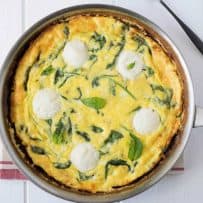 Frittata cooked in a pan with rounds of fresh ricotta and green spinach