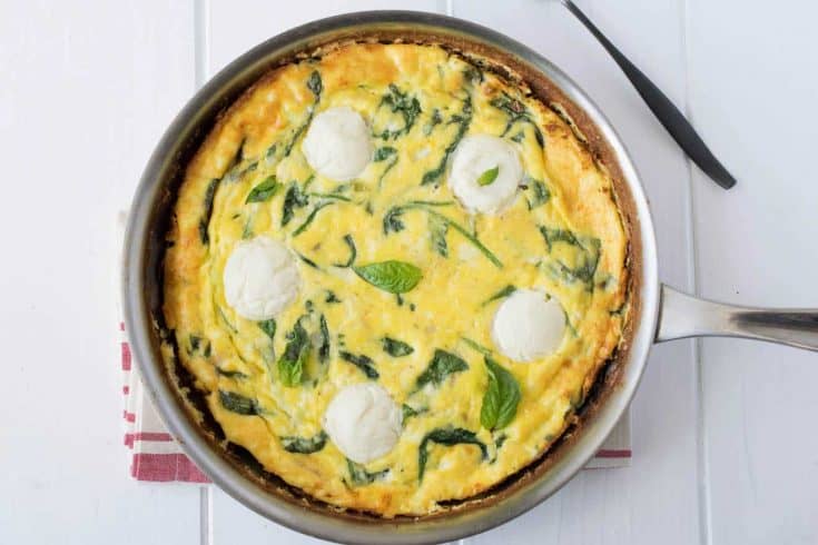 Frittata cooked in a pan with rounds of fresh ricotta and green spinach