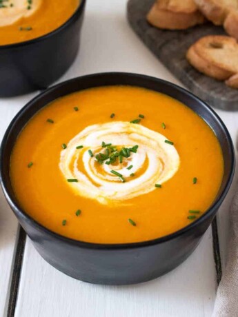 Roasted Carrot Ginger Soup in a black bowl with spoon and crusty bread