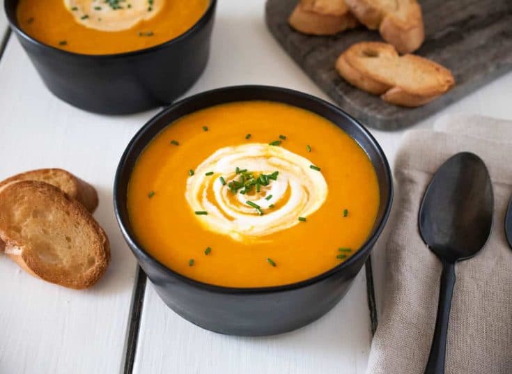 Roasted Carrot Ginger Soup in a black bowl with spoon and crusty bread