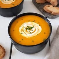 A bowl of Roasted Carrot Ginger Soup garnished with sour cream and chives