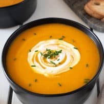 Green chopped chives and sour cream swirled onto the top of carrot soup