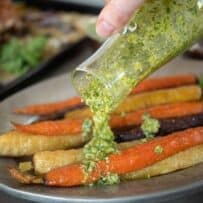 Pouring green pesto over roasted carrots