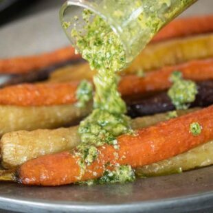 A closeup of pouring pesto over roasted carrots