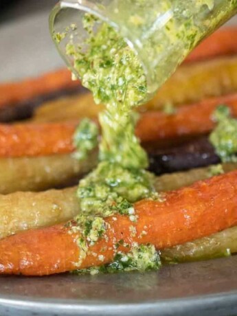 A closeup of pouring pesto over roasted carrots