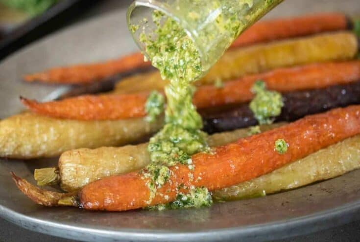 A closeup of pouring pesto over roasted carrots