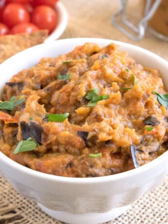 Roasted eggplant dip in a white bowl garnished with fresh parsley